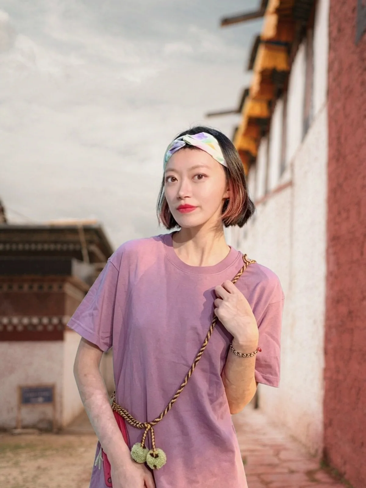 Nelly ZHUANG in a whitewashed monastery lane in Tibet, wearing a wurdoo chain across the body